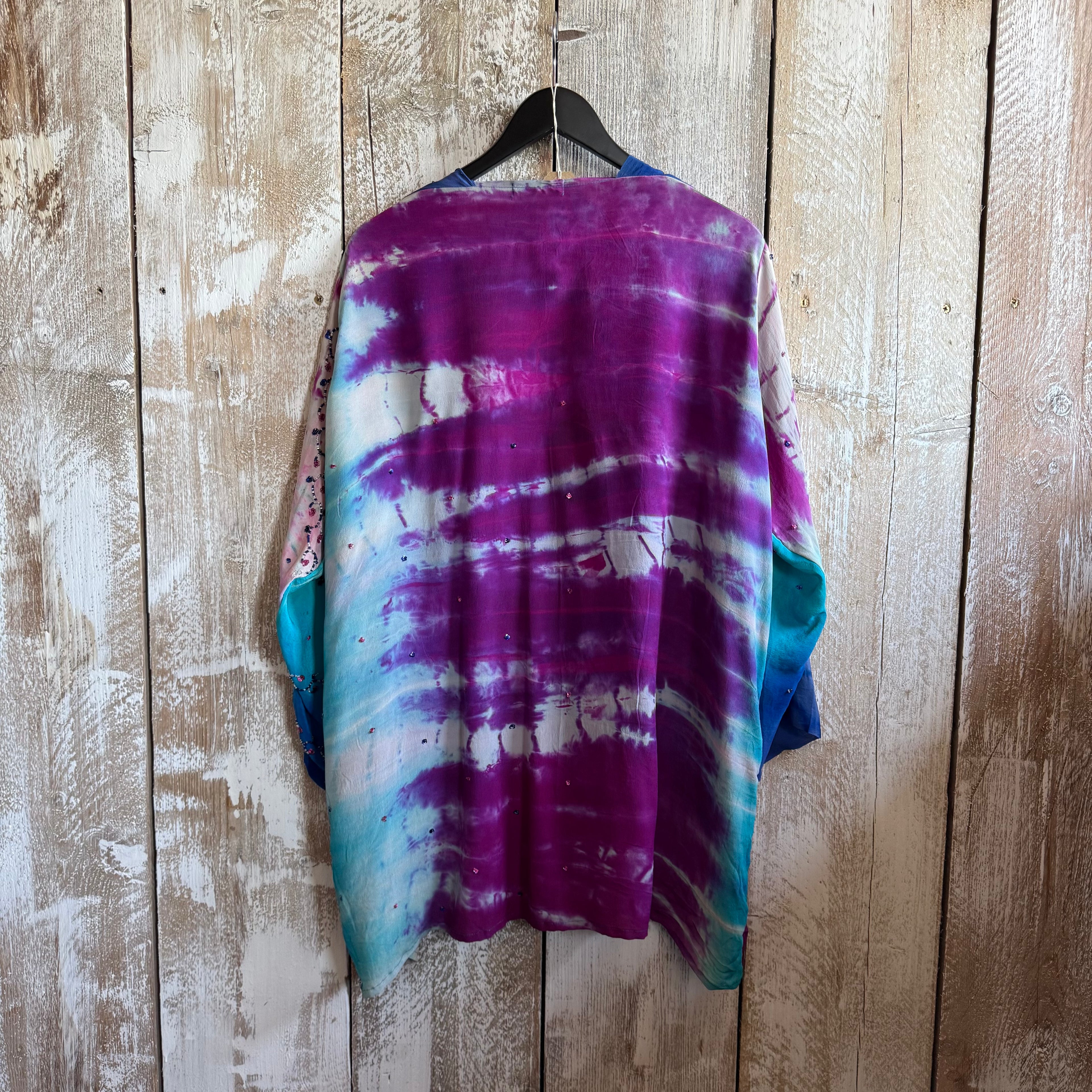 Tie-dye shirt on a hanger against a wooden wall