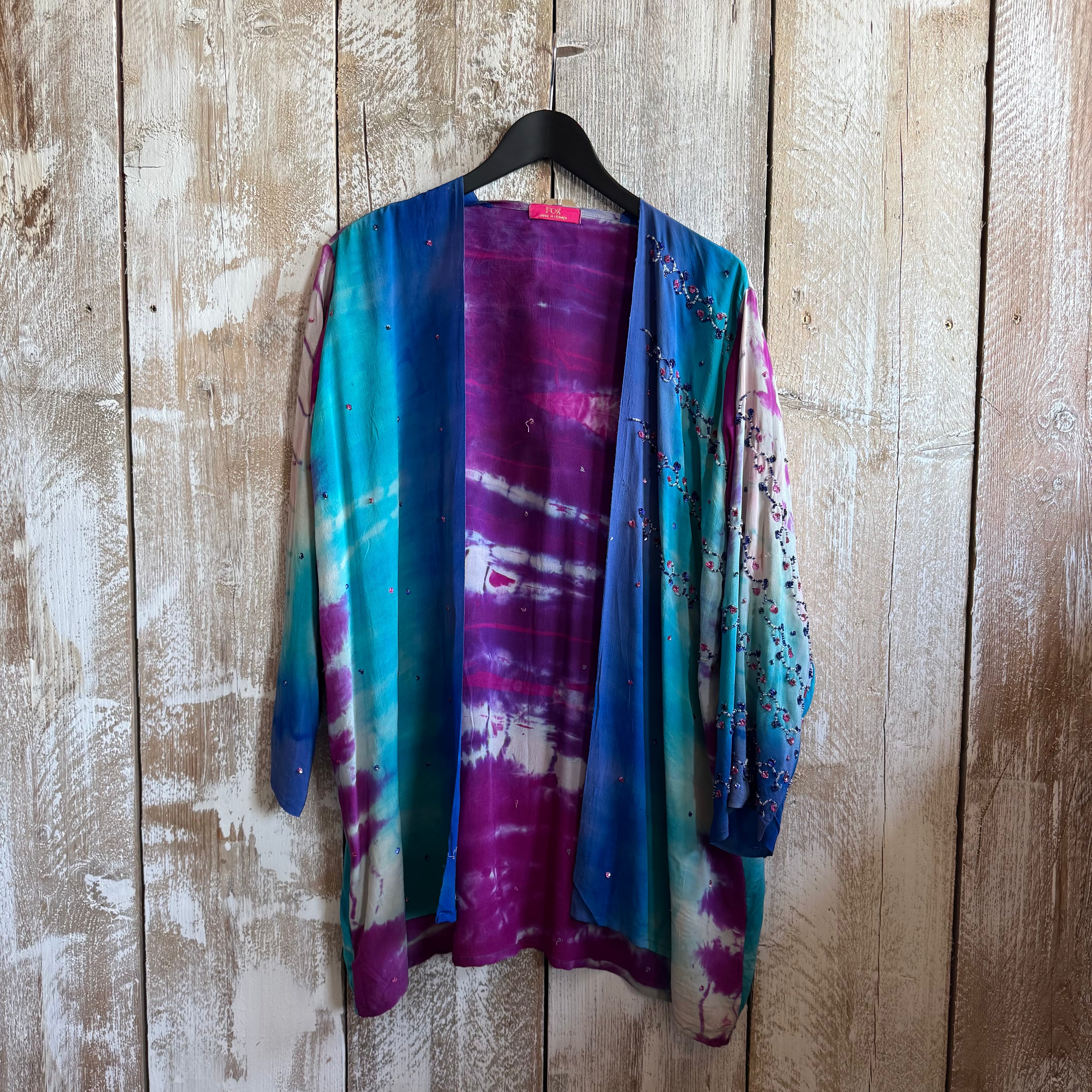 Colorful tie-dye shirt on a hanger against a wooden wall