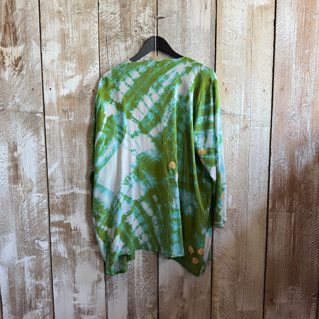 Green tie-dye shirt on a hanger against a wooden wall.