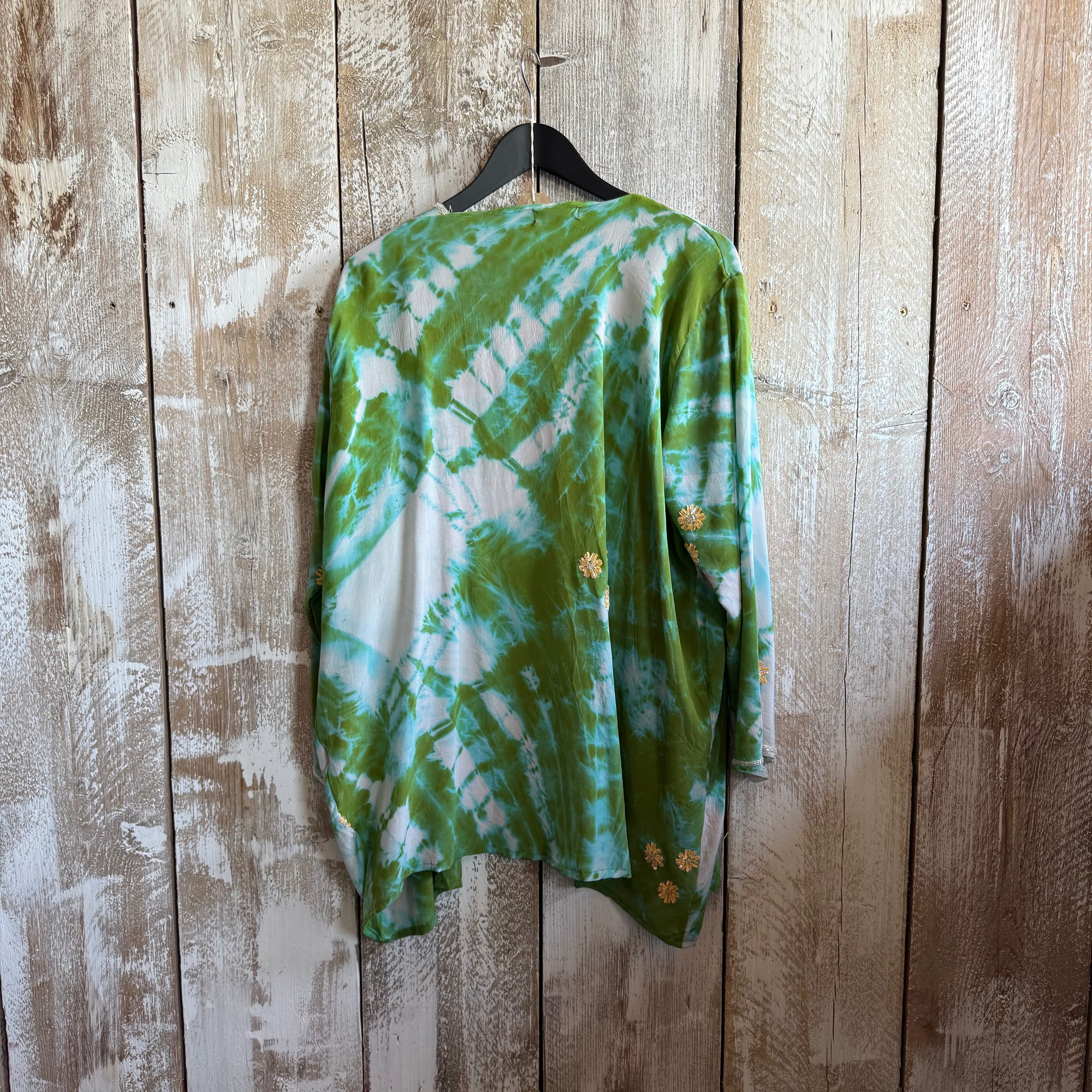 Green tie-dye shirt on a hanger against a wooden wall.
