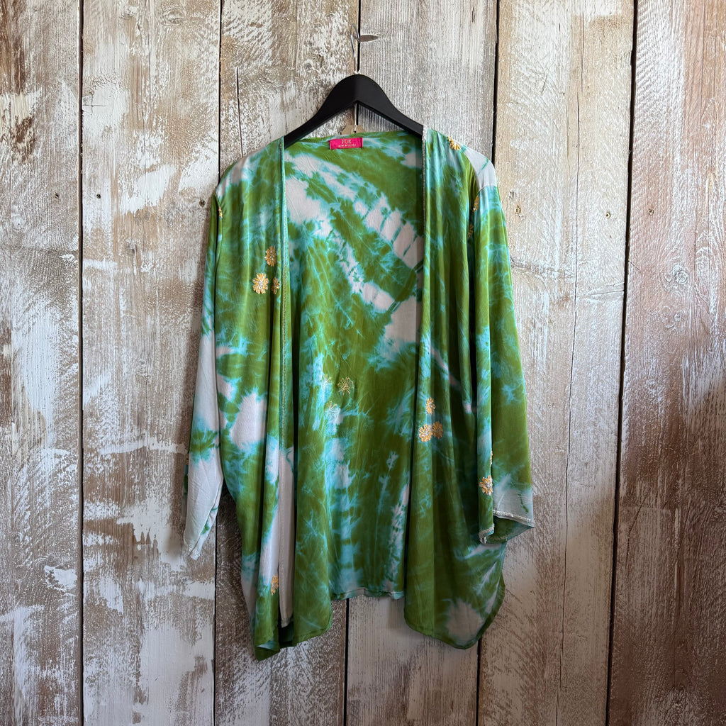 Green tie-dye shirt on a hanger against a wooden wall.