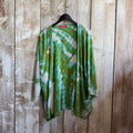 Green tie-dye shirt on a hanger against a wooden wall.