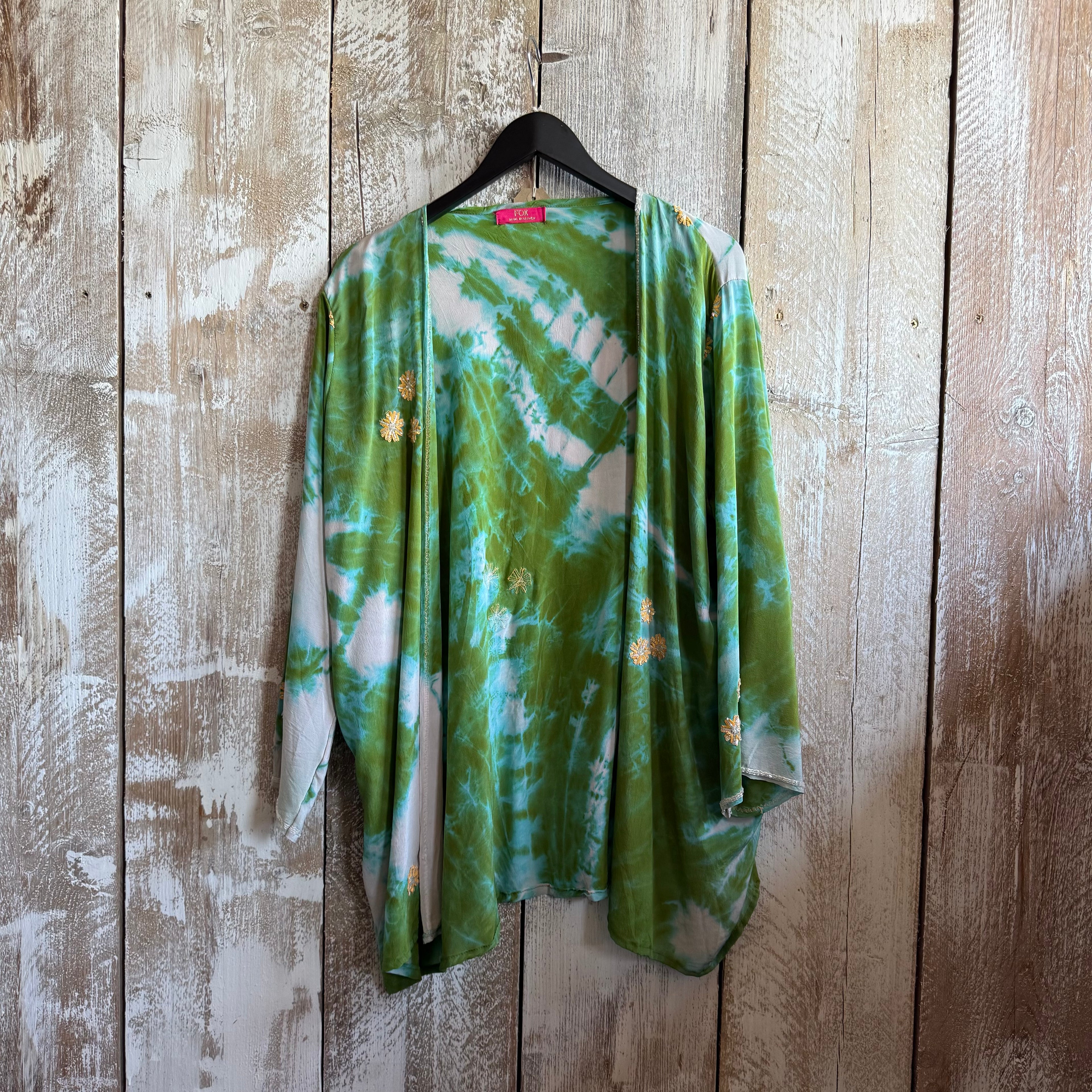 Green tie-dye shirt on a hanger against a wooden wall.