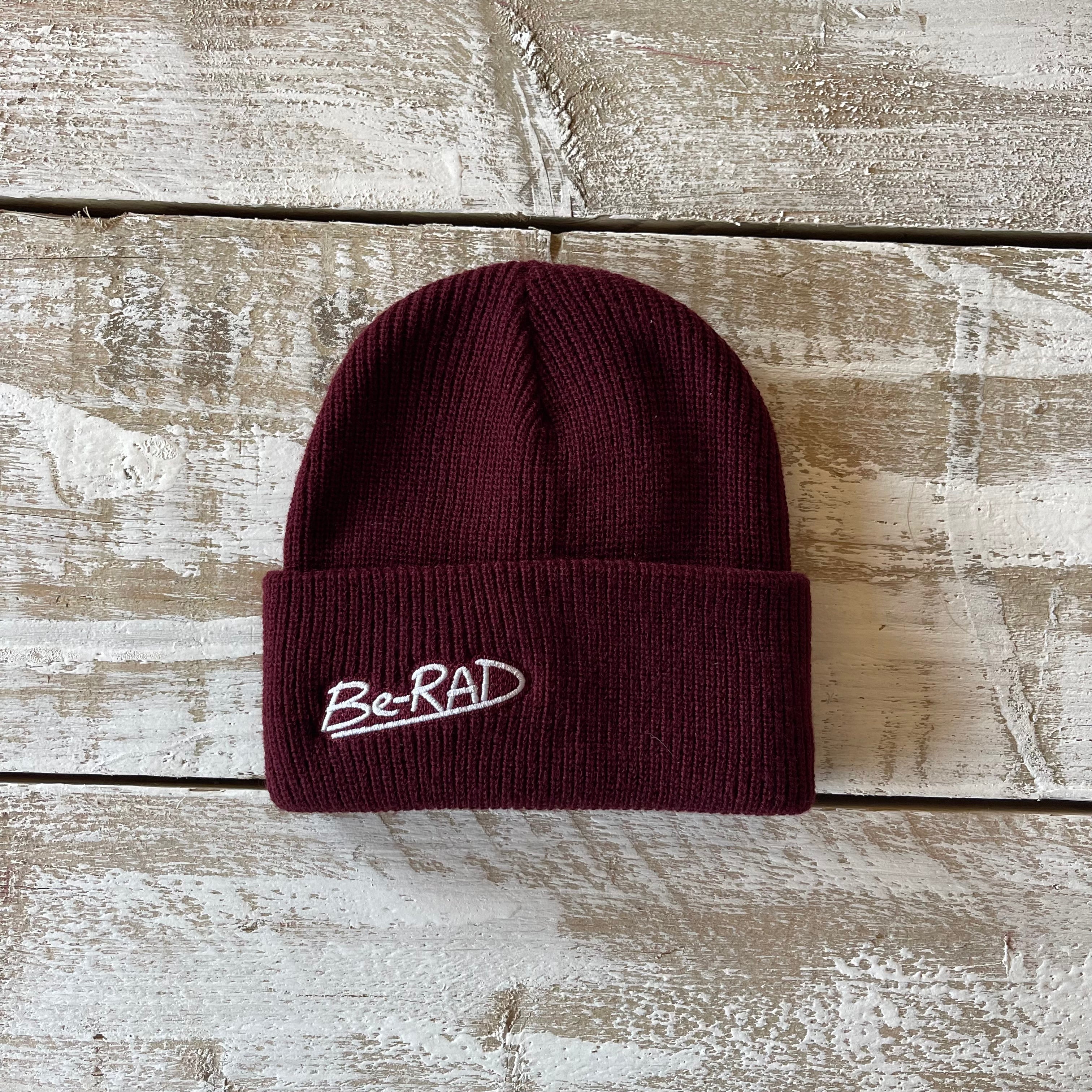 Maroon beanie with 'Be-RAD' logo on a wooden surface