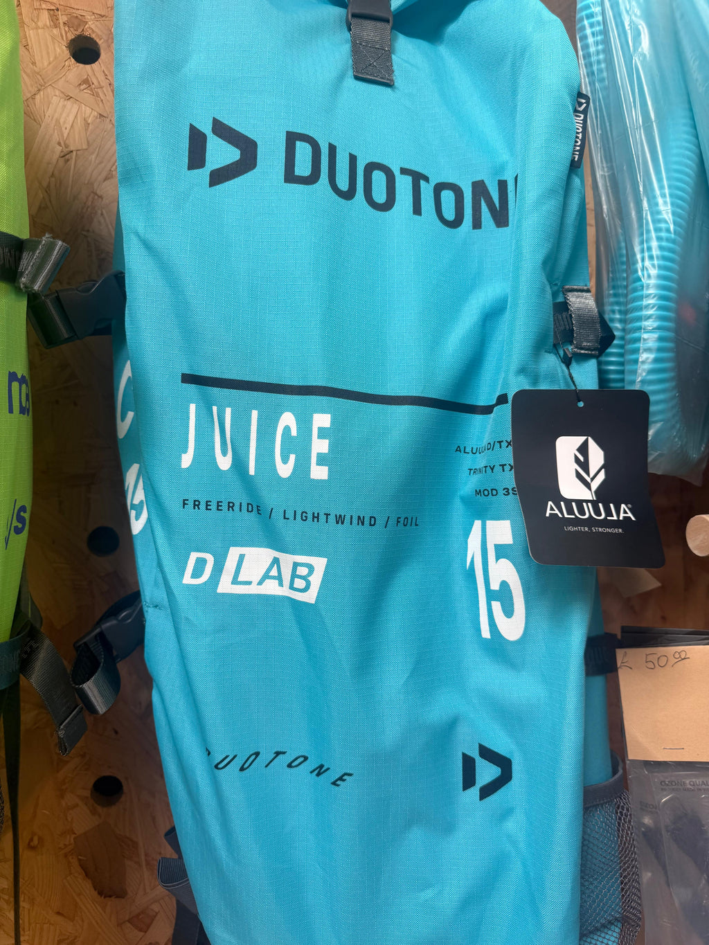 A turquoise blue Duotone Juice D-Lab 15m backpack shown hanging on a store rack with a black Aluula brand tag attached.