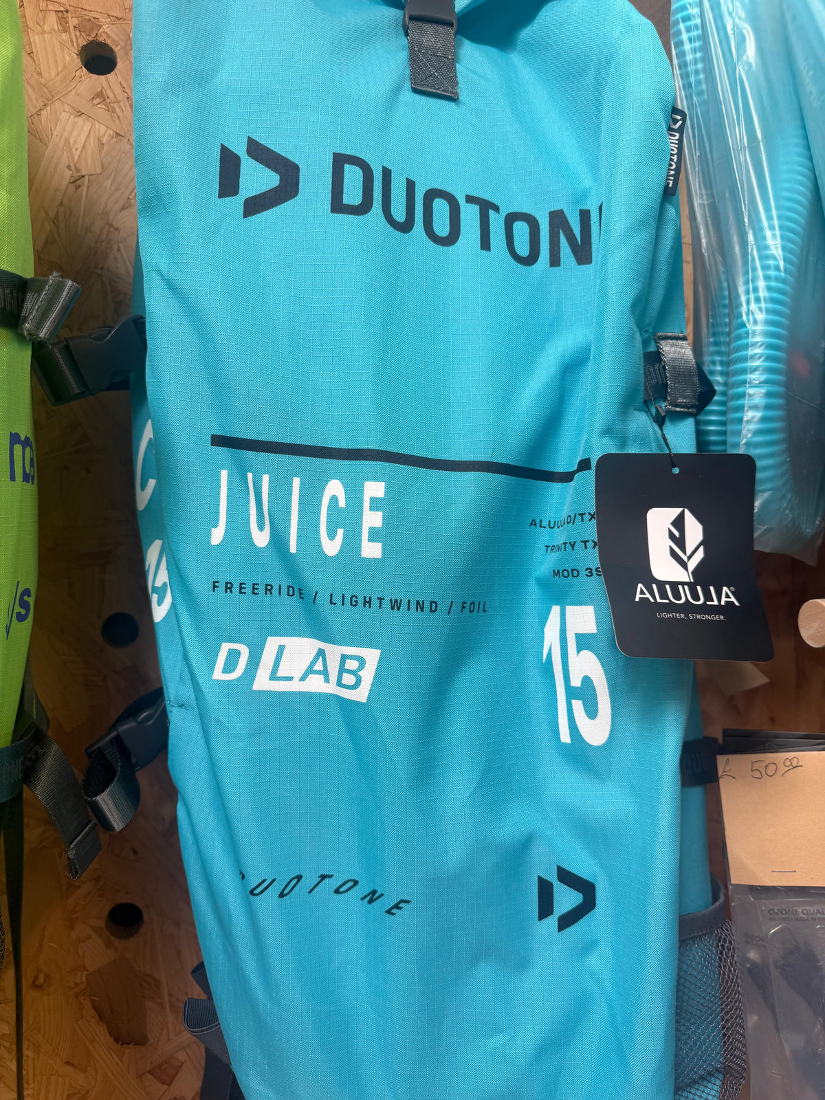 A turquoise blue Duotone Juice D-Lab 15m backpack shown hanging on a store rack with a black Aluula brand tag attached.
