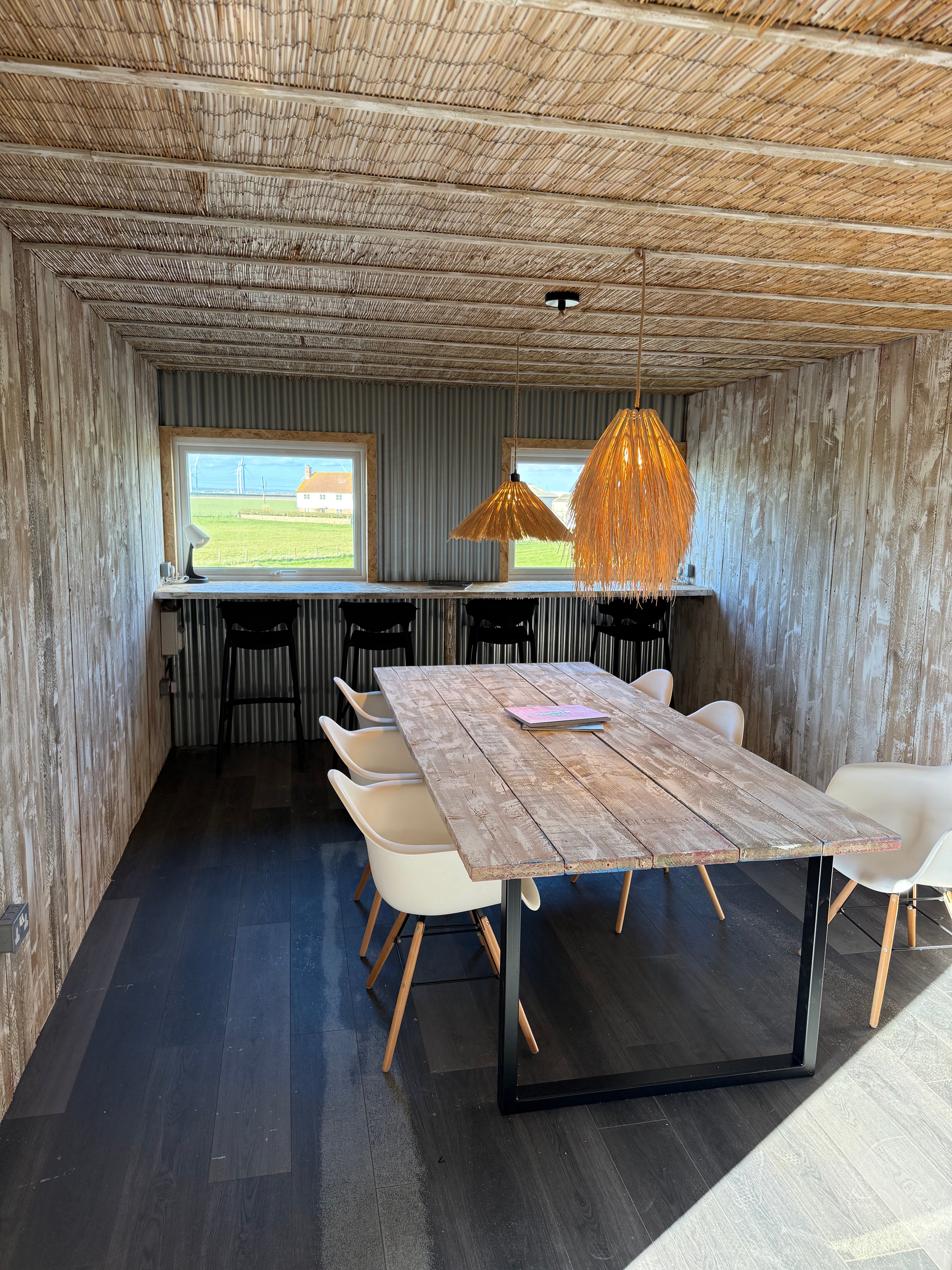 Co-working area with a wooden table and chairs in a rustic room with straw ceiling.
