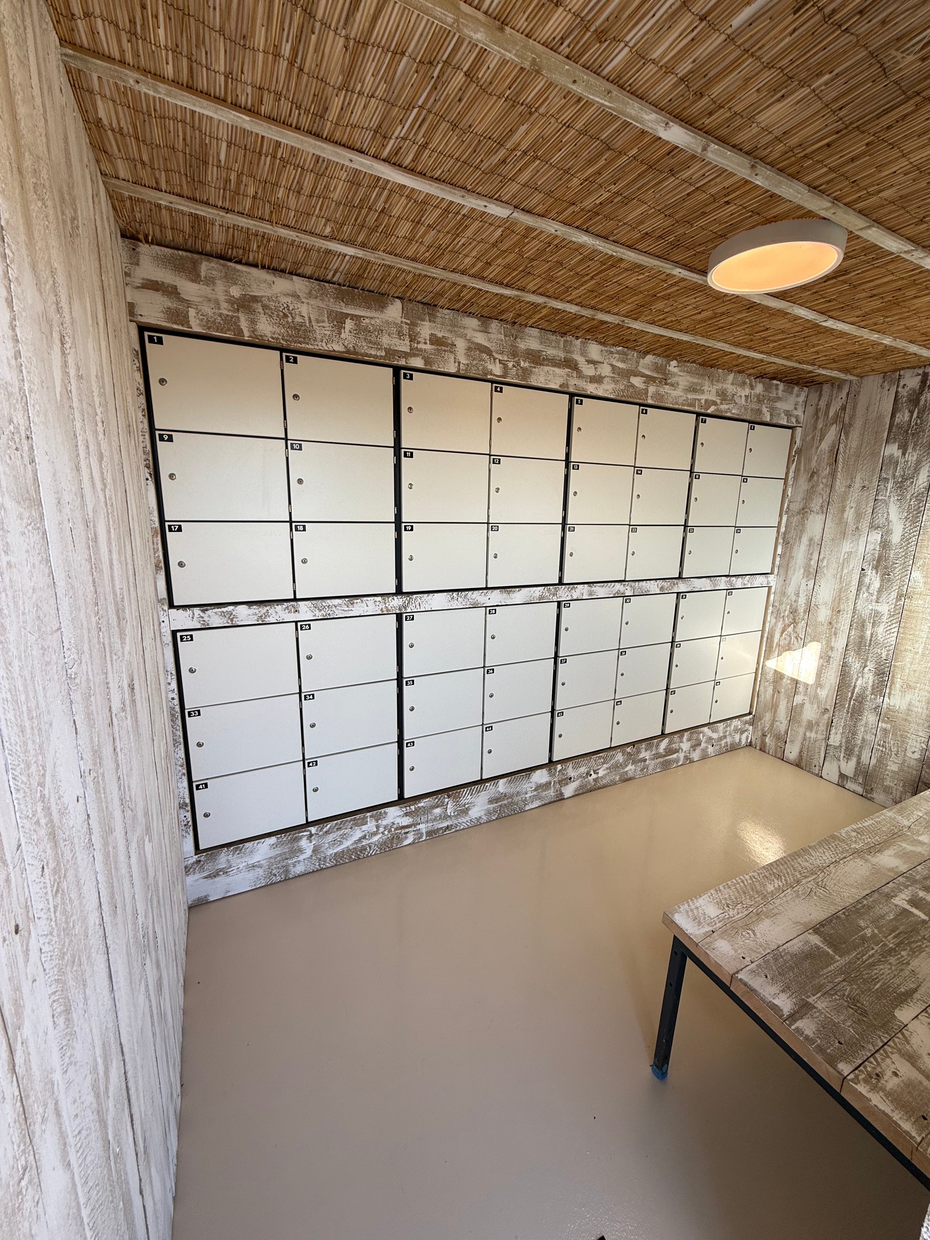 Room with rows of white lockers on a wall, wooden floor, and ceiling.