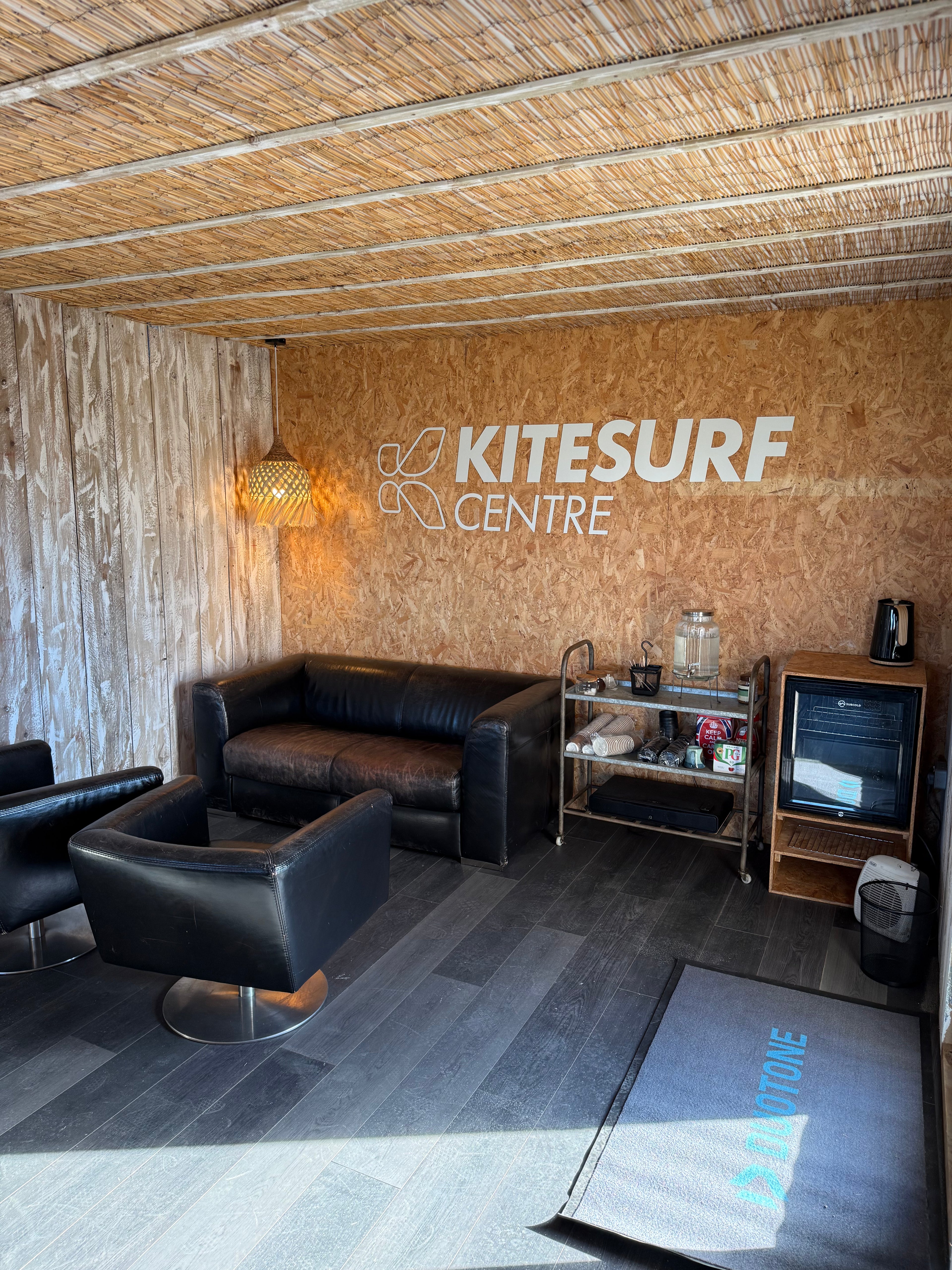 Interior of a kitesurf center with black leather furniture and wooden walls.